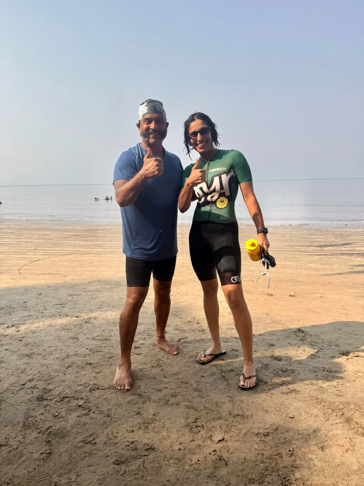 Divya in the green OYR prototype trisuit at the beach with a fellow athlete.